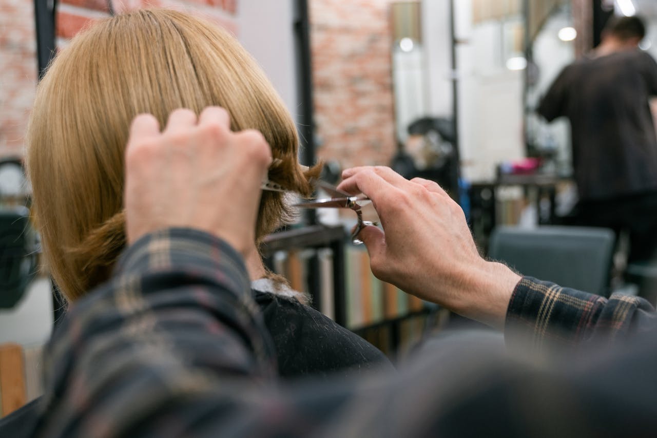 services-07 Hairdresser cutting woman's blonde hair in salon with scissors and mirror.